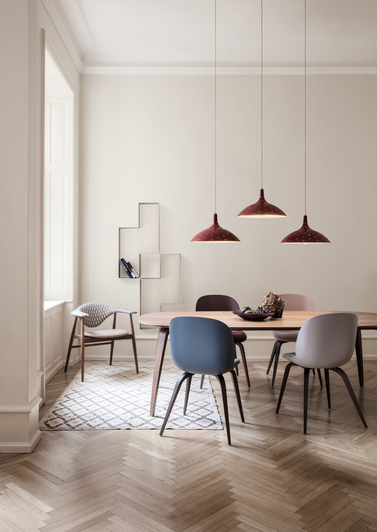 Vriendelijke en moderne eethoek van het merk GUBI. De gekleurde Beetle stoelen en de Masculo eetkamerstoel in de hoek hebben vrolijke ronde vormen. De GUBI eettafel heeft een tafelblad met ronde hoeken en gebogen tafelpoten.